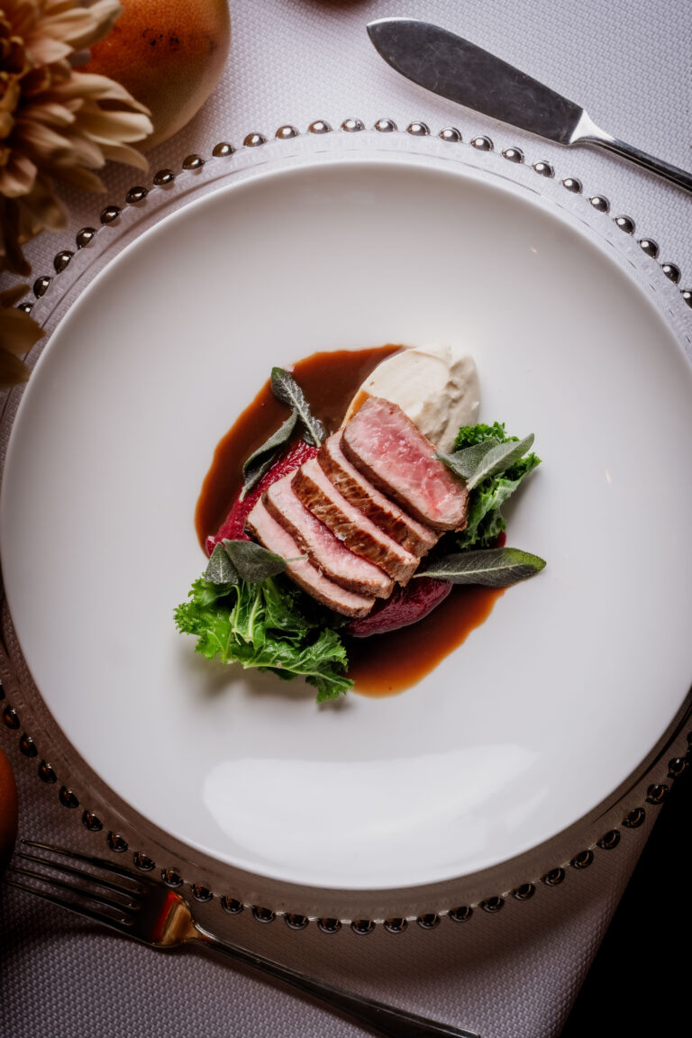 Sliced gourmet meat with sauce and greens served as part of a fine dining private catering menu.